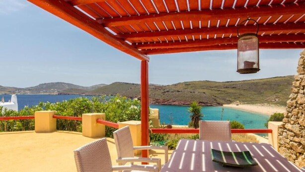 A terrace with wicker chairs and a table, overlooking a coastal landscape with a clear view of the sea and distant hills. - Villa 'Agios Sostis Mykonos' with Sea View, Wi-Fi and Air Conditioning (Mýkonos City)