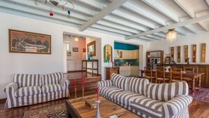 A spacious living area with striped sofas, a wooden coffee table, and a dining area with a wooden table and chairs. - Villa 'Agios Sostis Mykonos' with Sea View, Wi-Fi and Air Conditioning (Mýkonos City)