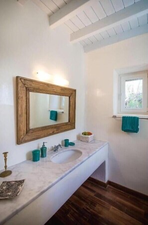 Un baño con un espejo de marco de madera, un lavabo blanco y una ventana con una toalla colgada en la pared.