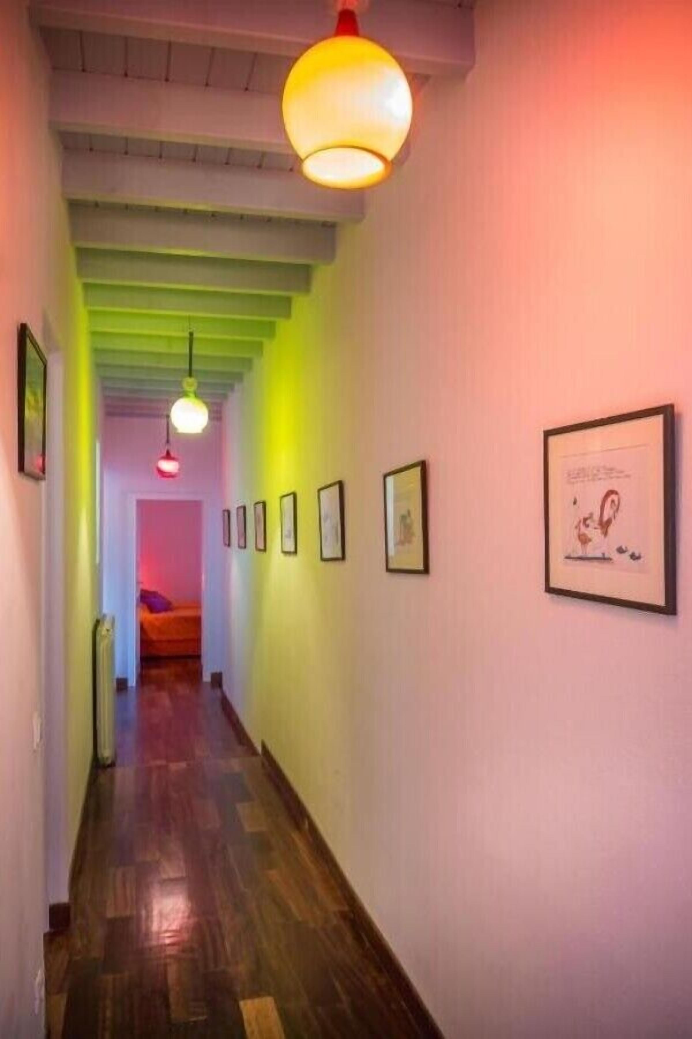 A hallway with wooden flooring, framed artwork on the walls, and hanging pendant lights.