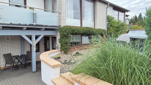Uma casa moderna com varanda, mobiliário de jardim e área verde com plantas e um caminho.