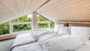Une chambre avec un plafond en pente et une grande fenêtre donnant sur un espace verdoyant.