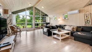 Un salon spacieux avec une grande fenêtre, un canapé noir, une table basse blanche et un meuble TV en bois.