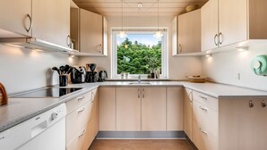 Une cuisine moderne avec des meubles de couleur bois clair, un îlot central doté d’un évier et une vue sur la verdure à l’extérieur.