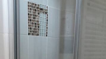 Une douche fermée par des parois en verre, dotée d’un pommeau de douche à main et d’un panneau de commande fixé au mur.