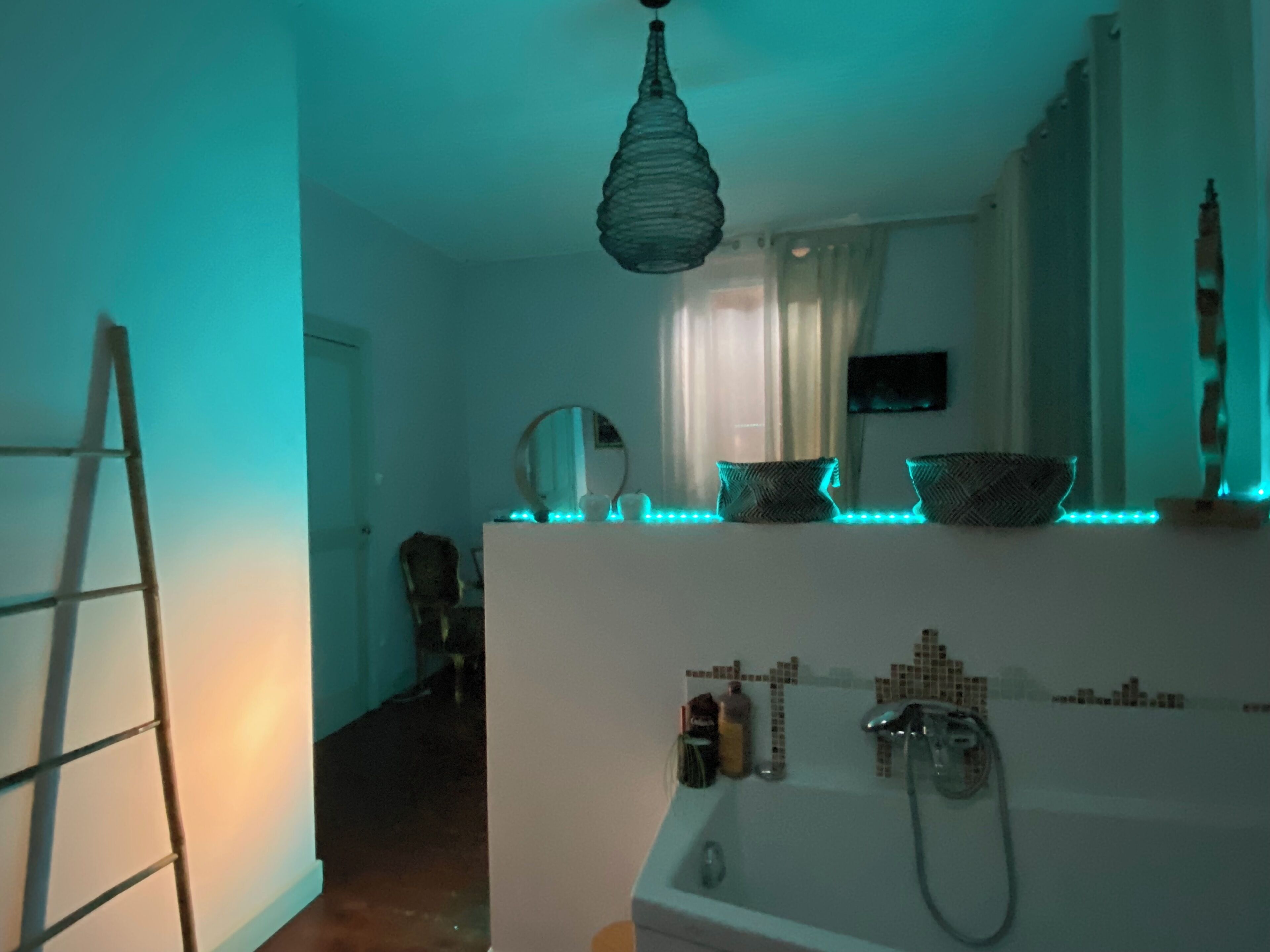 Une salle de bain avec une baignoire, une douche et un lavabo. Une échelle est appuyée contre le mur et un miroir est placé au-dessus du lavabo.