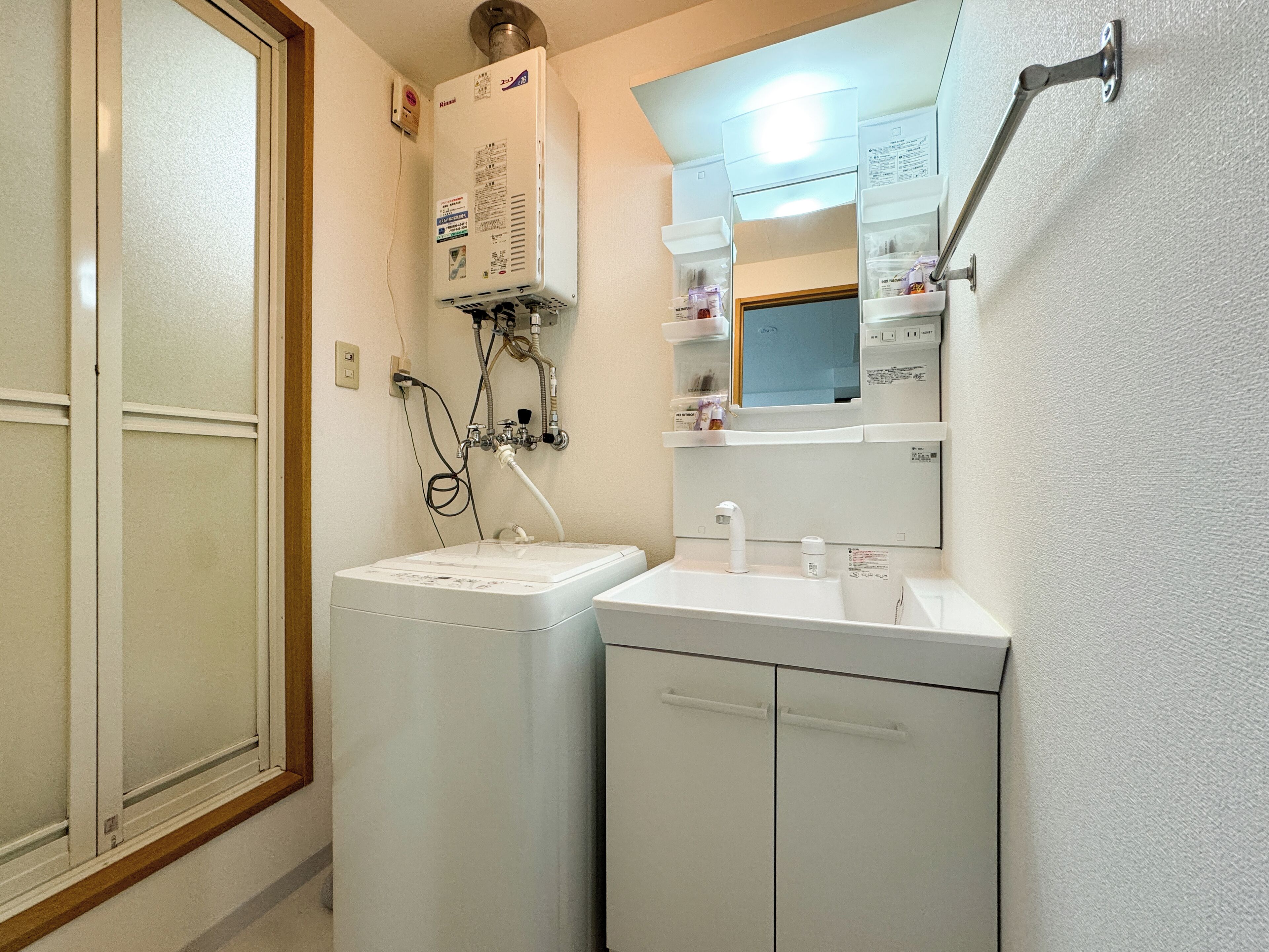 A compact bathroom with a washing machine, a sink, and a mirror.