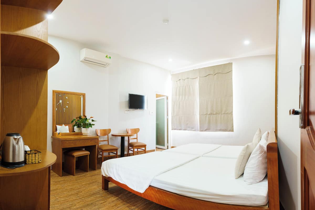 Habitación de hotel con cama, escritorio, silla, televisión y ventana con cortinas.