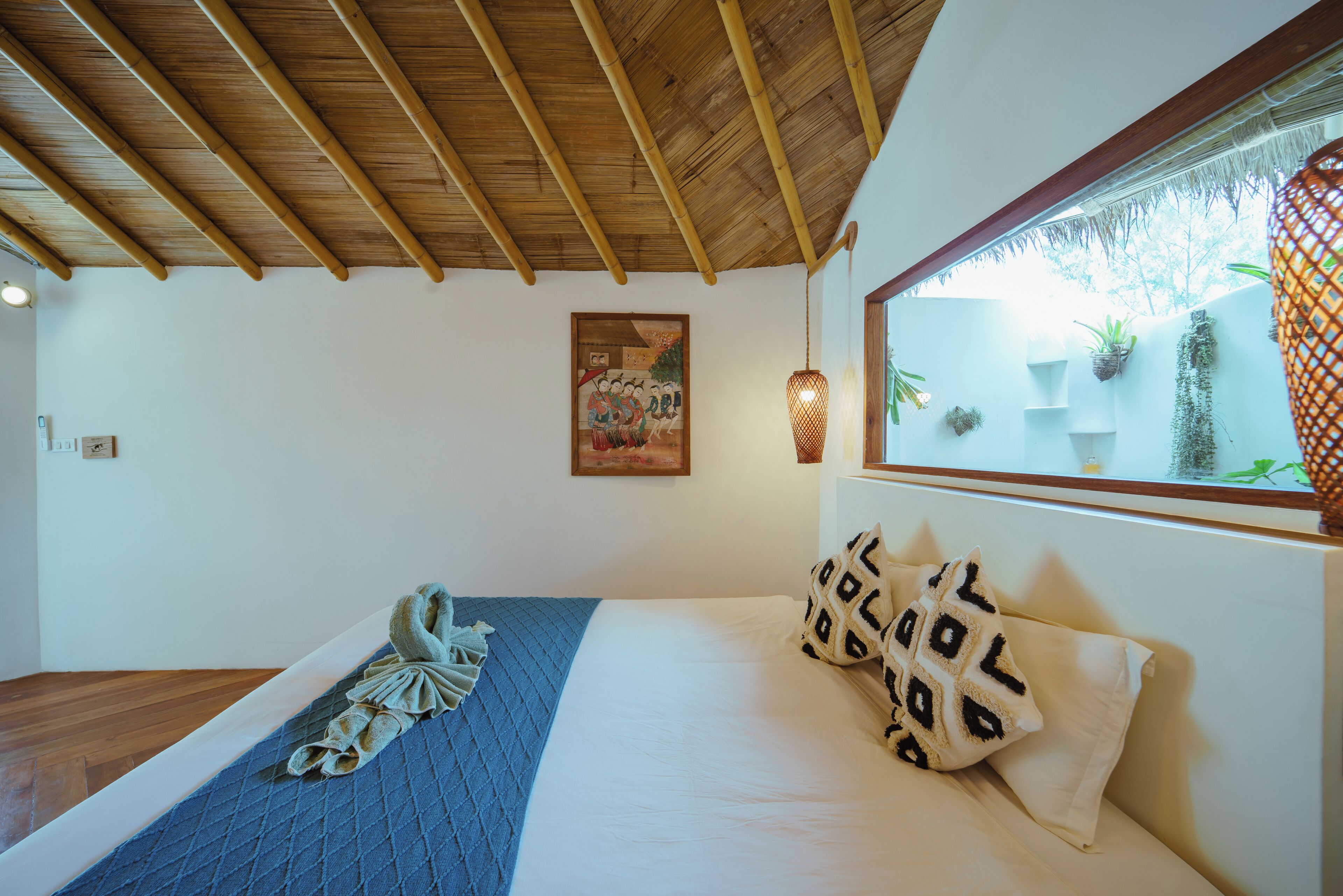 A bedroom with a wooden ceiling, a bed with a blue blanket, and a window with potted plants.