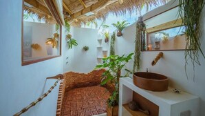 Une salle de bain avec un sol carrelé imitant un motif de briques, une grande fenêtre, un plafond en bois et diverses plantes.