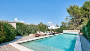 A rectangular pool with clear blue water, surrounded by a wooden deck and lounge chairs with umbrellas. - Villa Montagne by Interhome (Oppede)