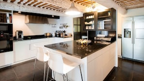 A modern kitchen with a central island, white bar stools, stainless steel appliances, and a wooden ceiling. - Villa Montagne by Interhome (Oppede)