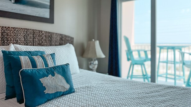 Une chambre d’hôtel avec un lit, des oreillers, une lampe et une vue sur l’océan depuis un balcon.
