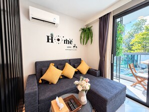 Una sala de estar moderna con un sofá gris, cojines amarillos, un reloj de pared y una planta en maceta.
