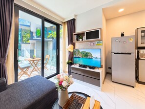 Una sala moderna con un sofá, una televisión, un comedor con mesa y sillas, y una zona de cocina con refrigerador y microondas.