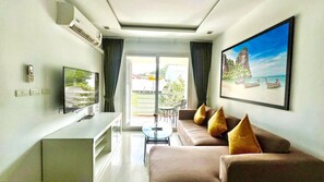 A modern living room with a sofa, TV, and a painting of a beach scene. - 6-17 - 2 Bdr Condo with Balcony and shared Pool (Tambon Patong)