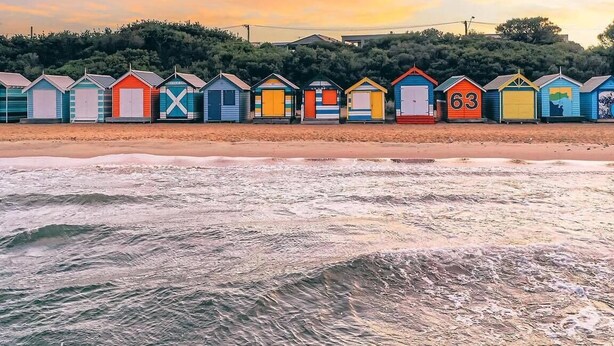 A row of colorful beach huts with a beach and ocean in the foreground. - Brighton Blissful | Family Poolside Vila Pool Spa Sauna (Brighton East)