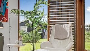 Una sala de estar moderna con un sillón de cuero blanco, una mesita pequeña, una lámpara de pie y un ventanal con persianas.