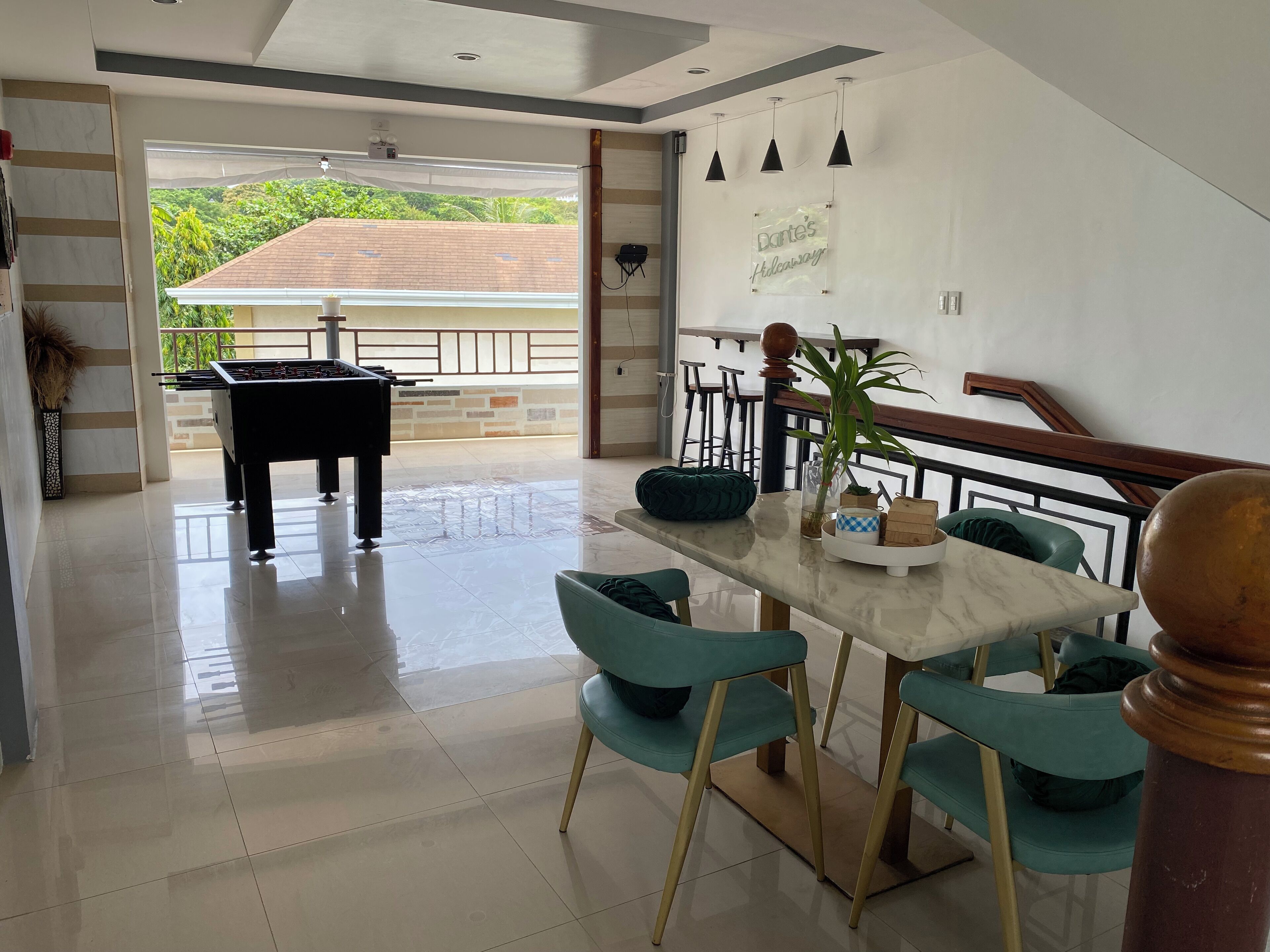 A spacious room with a foosball table, a dining table with chairs, and a view of greenery outside.