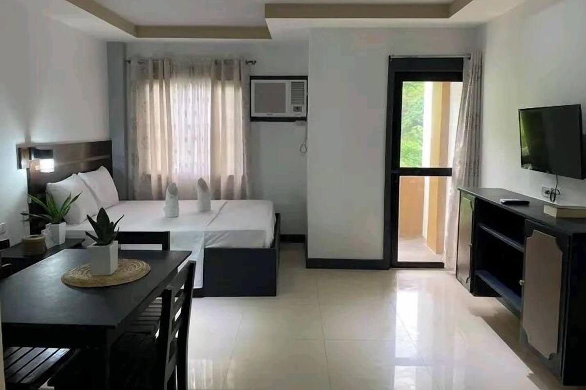 Ein modernes Hotelzimmer mit Bett, Fernseher, Esstisch und Balkon.