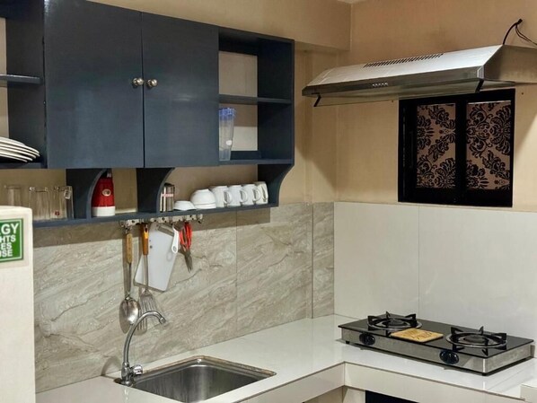 Una cocina con estufa a gas, pileta de acero inoxidable, alacenas oscuras y un salpicadero decorativo.