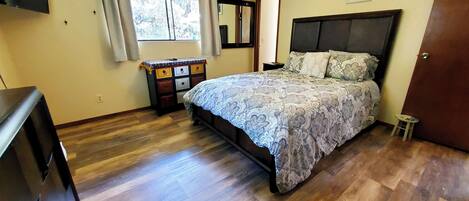 Un dormitorio con cama, cómoda, ventilador de techo y ventana con cortinas.