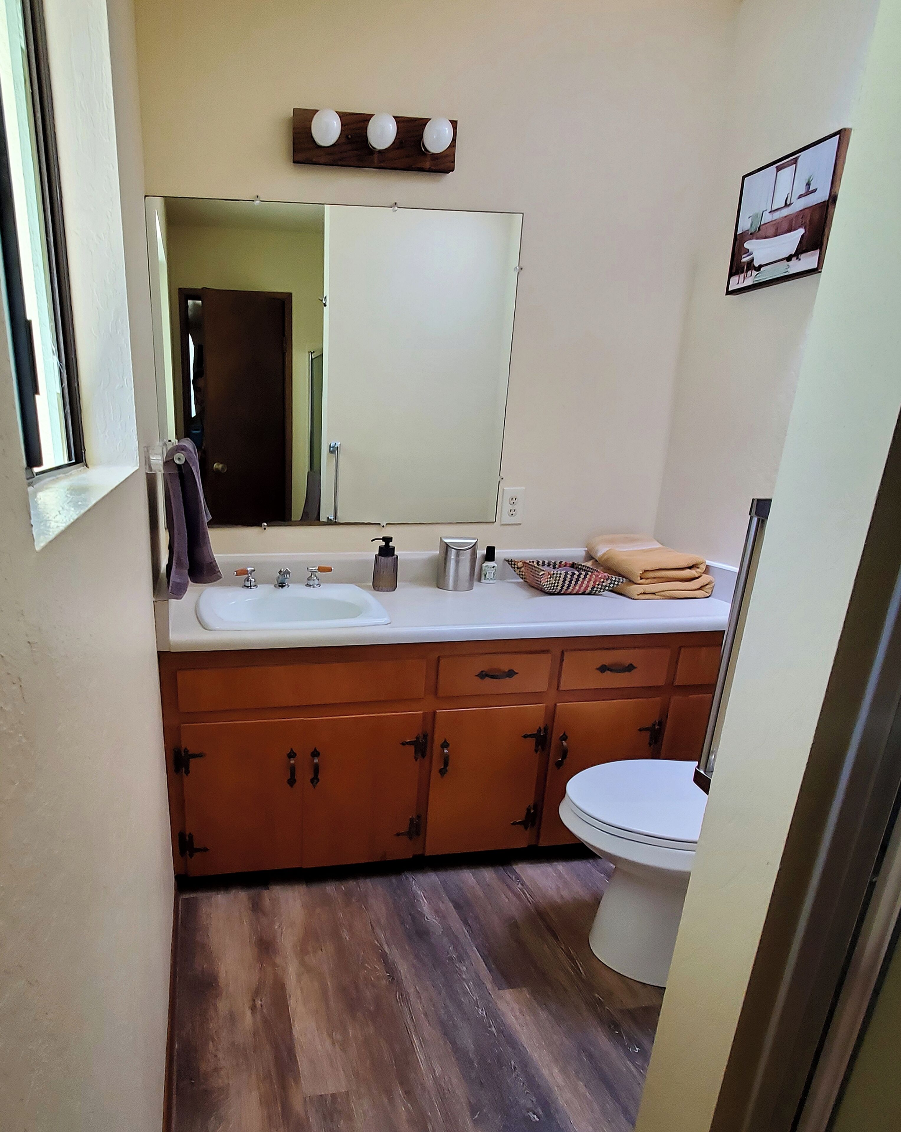 A compact bathroom with a white sink, wooden cabinets, a toilet, and a mirror above the sink.