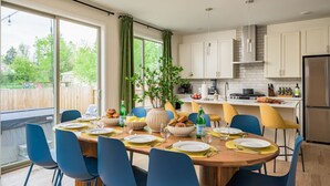 A modern kitchen with white cabinets, a dining table set for six, and a large window with curtains. - Hot Tub | Rooftop | Game Room | 5 Bathrooms (Denver)