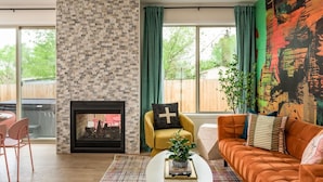 Un salon avec une cheminée, un canapé, une table basse et une grande fenêtre avec des rideaux.
