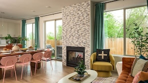 Un salon moderne avec une cheminée, un coin repas avec des chaises roses et de grandes fenêtres avec des rideaux.