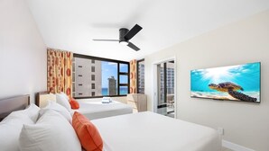 Una habitación de hotel con dos camas, un ventilador de techo, un ventanal grande con vista a la ciudad y un cuadro con una tortuga marina.