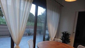 A room with a round wooden table and four white wicker chairs. - Atenea House (Caldes de Malavella)