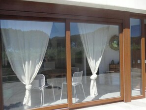Una habitación moderna con grandes puertas de vidrio correderas, cortinas blancas y un comedor con sillas y una mesa.