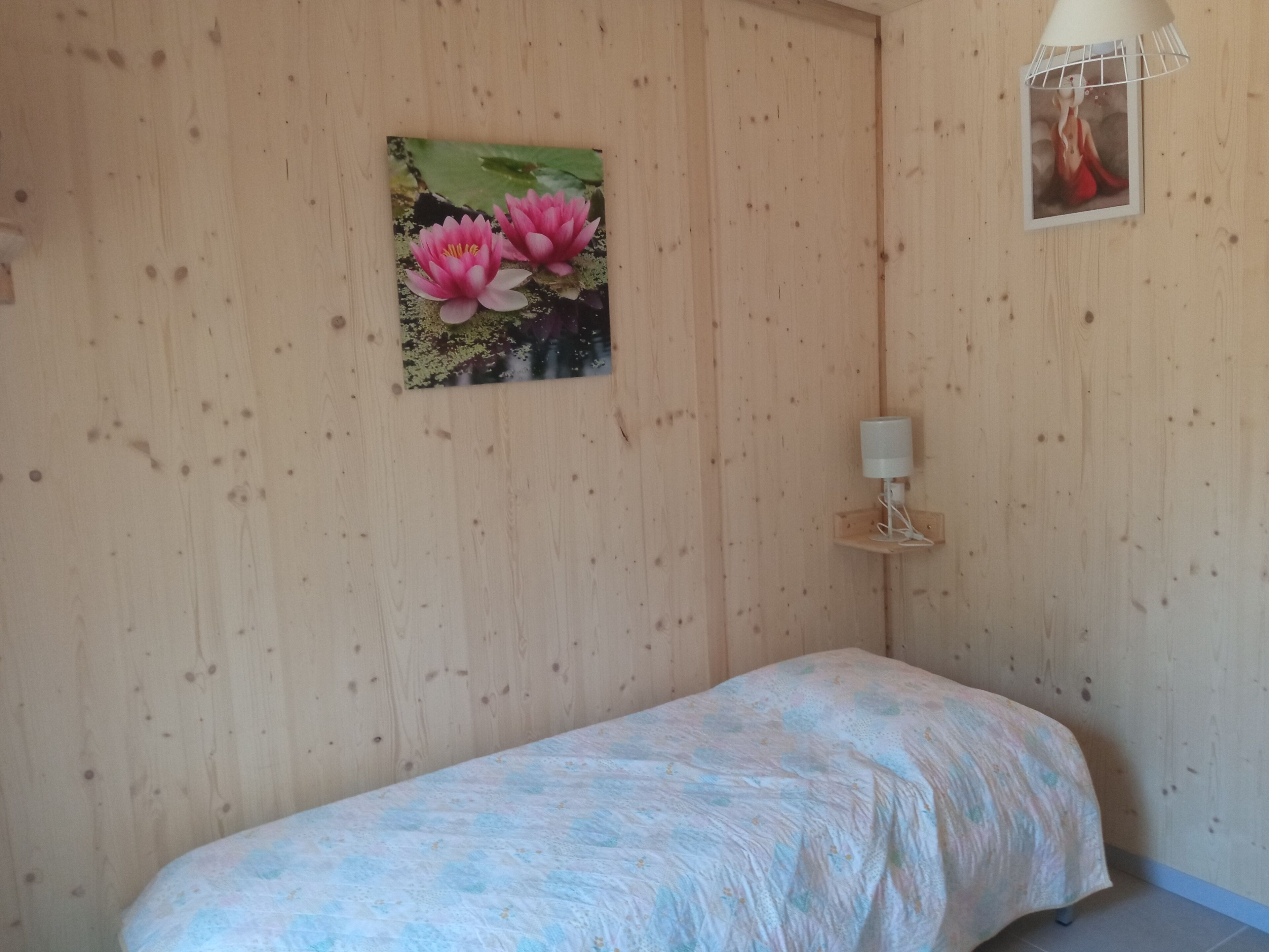A bedroom with a bed, a wall-mounted lamp, and a painting of pink flowers.