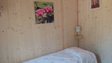 A bedroom with a bed, a wall-mounted lamp, and a painting of pink flowers.