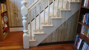 A staircase with white balusters and a wooden handrail, flanked by bookshelves filled with books. - Pretty Old House in Newport (Newport)