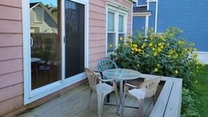 A patio with a table and chairs, a sliding glass door, and a yellow flowering bush. - Pretty Old House in Newport (Newport)