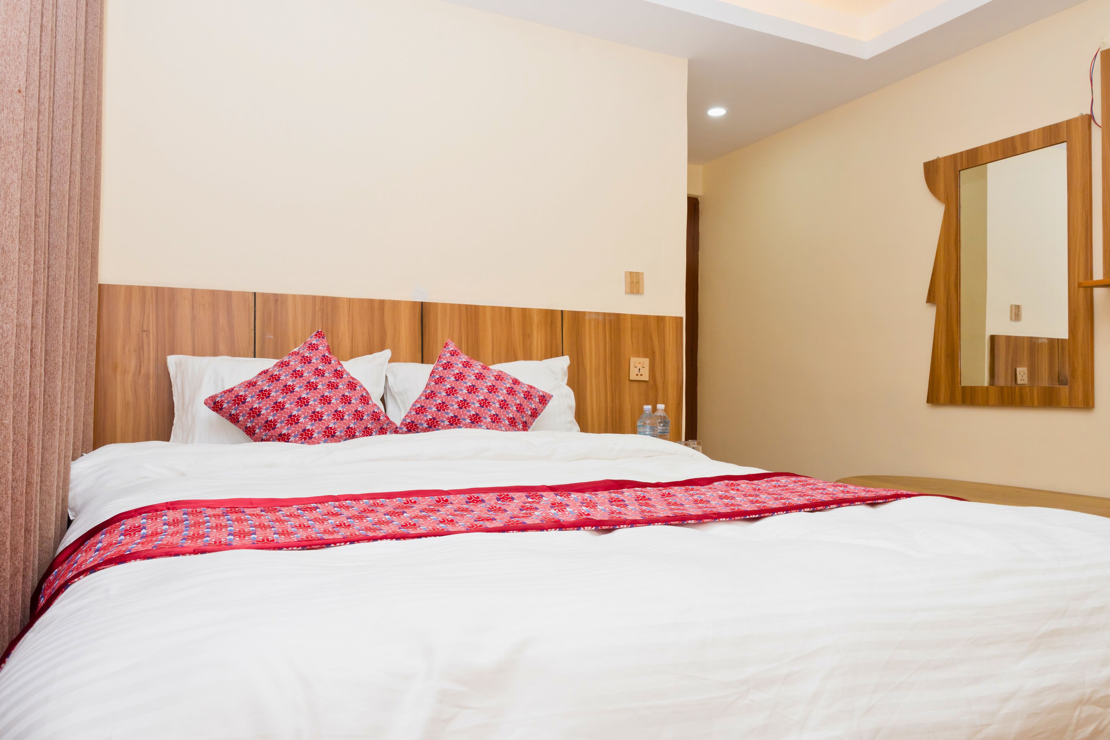 A hotel room with a large bed, white bedding, and a wooden headboard. There are two pillows with a red floral pattern.