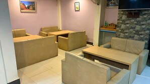 A room with beige sofas and tables, a flat-screen TV mounted on a stone wall, and artwork on the walls. - Rightway Hotel & Restaurant (Kathmandu)