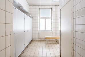 Un lavabo amb parets de rajola blanca, una banca i una finestra amb persianes.