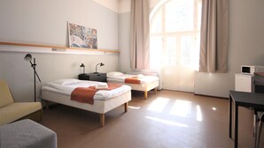 Habitación de hotel con dos camas, un escritorio, una silla, un sofá, una lámpara, un cuadro y una ventana con cortinas.