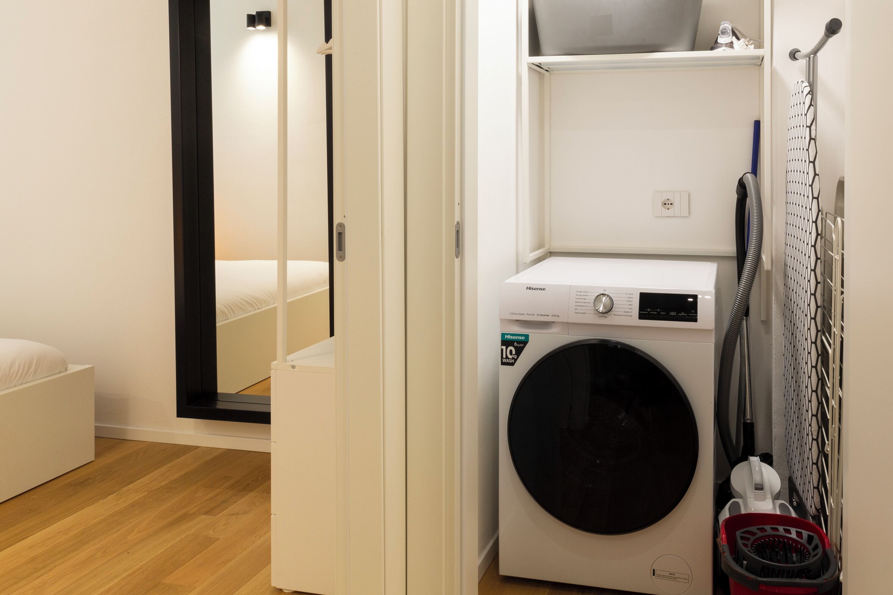A compact laundry area with a front-loading washing machine, a drying rack, and a small shelf above the machine.
