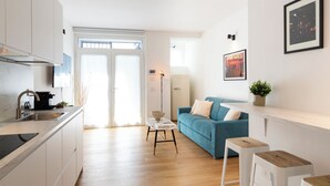 A modern kitchen with a sink, stove, and cabinets, a blue sofa with cushions, a small table, and a plant on the wall. - notaMi - Govone Fashion House (Milan)