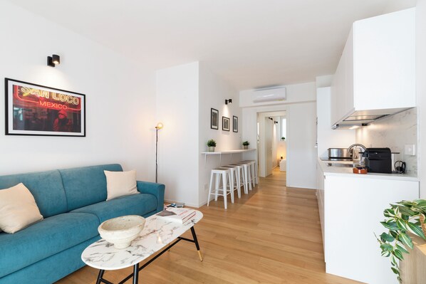 A modern living room with a blue sofa, a marble coffee table, and a kitchen area with white cabinets and a black stove. - notaMi - Govone Fashion House (Milan)