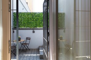 A small outdoor balcony with a wooden table and chairs, a potted plant, and a green hedge in the background. - notaMi - Govone Fashion House (Milan)