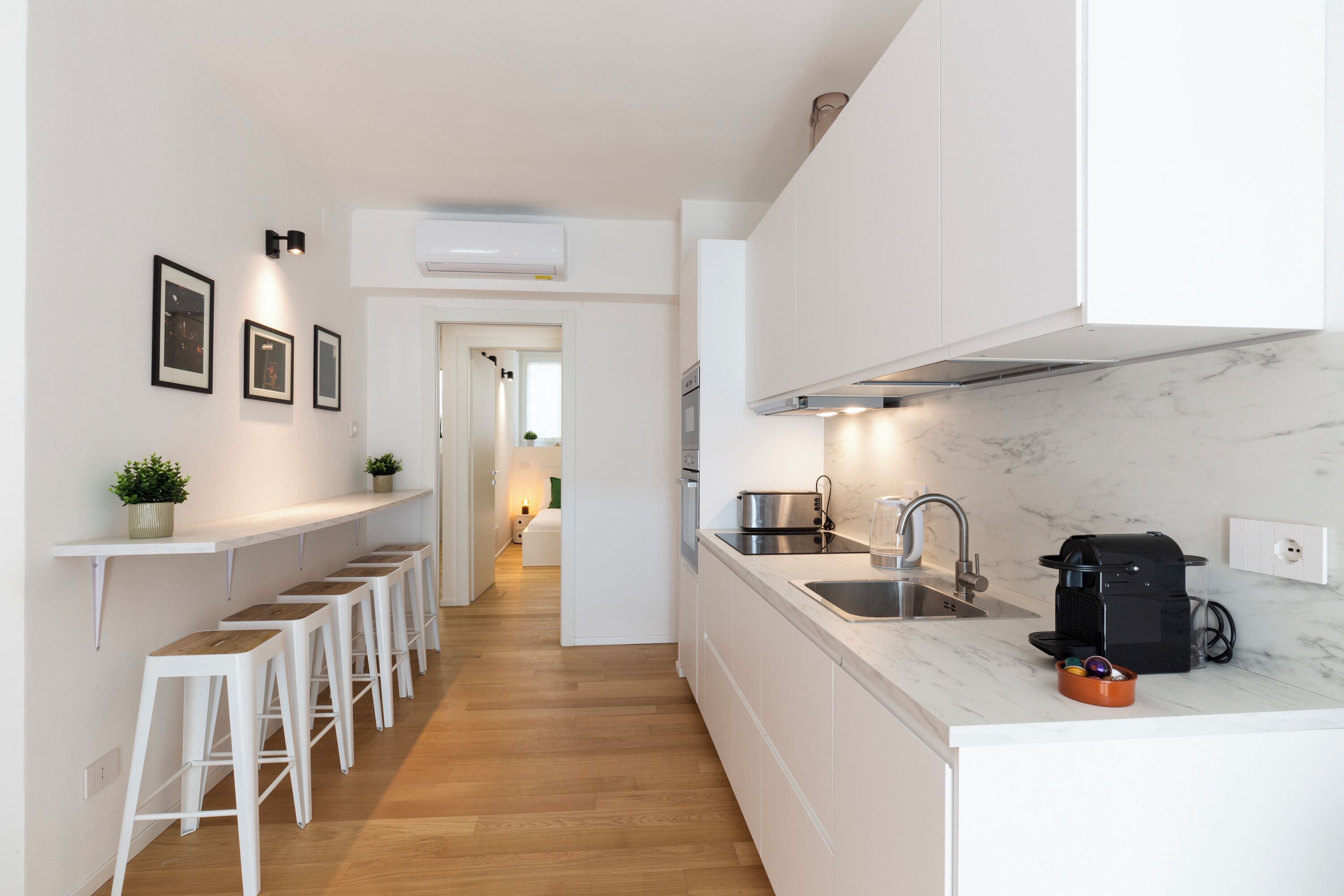 A modern kitchen with white cabinets, a marble countertop, and a coffee machine.