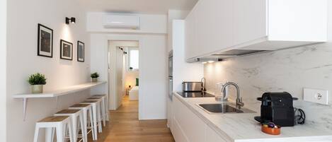 A modern kitchen with white cabinets, a marble countertop, and a coffee machine.