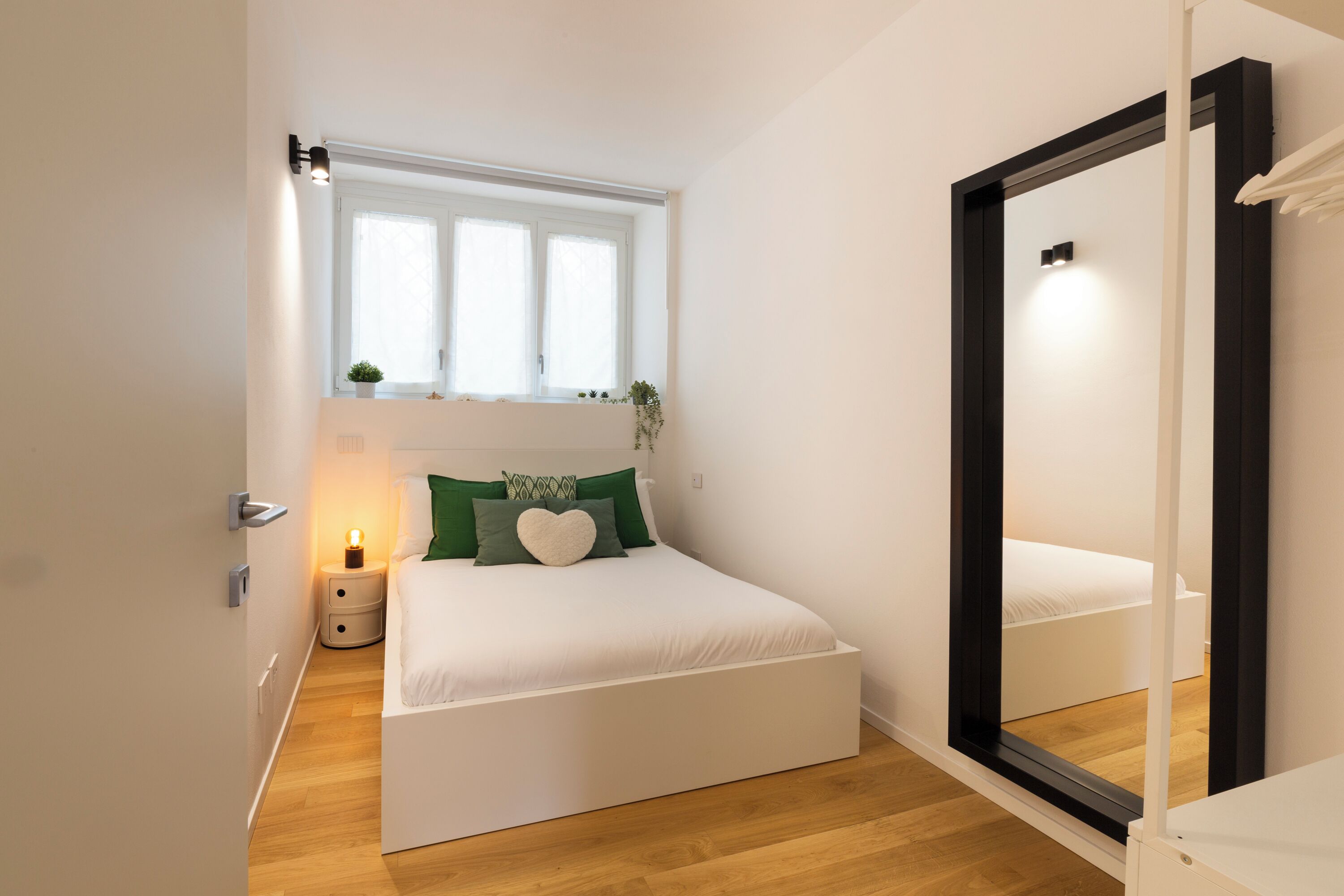 Una camera da letto con un letto, comodino, finestra e specchio.