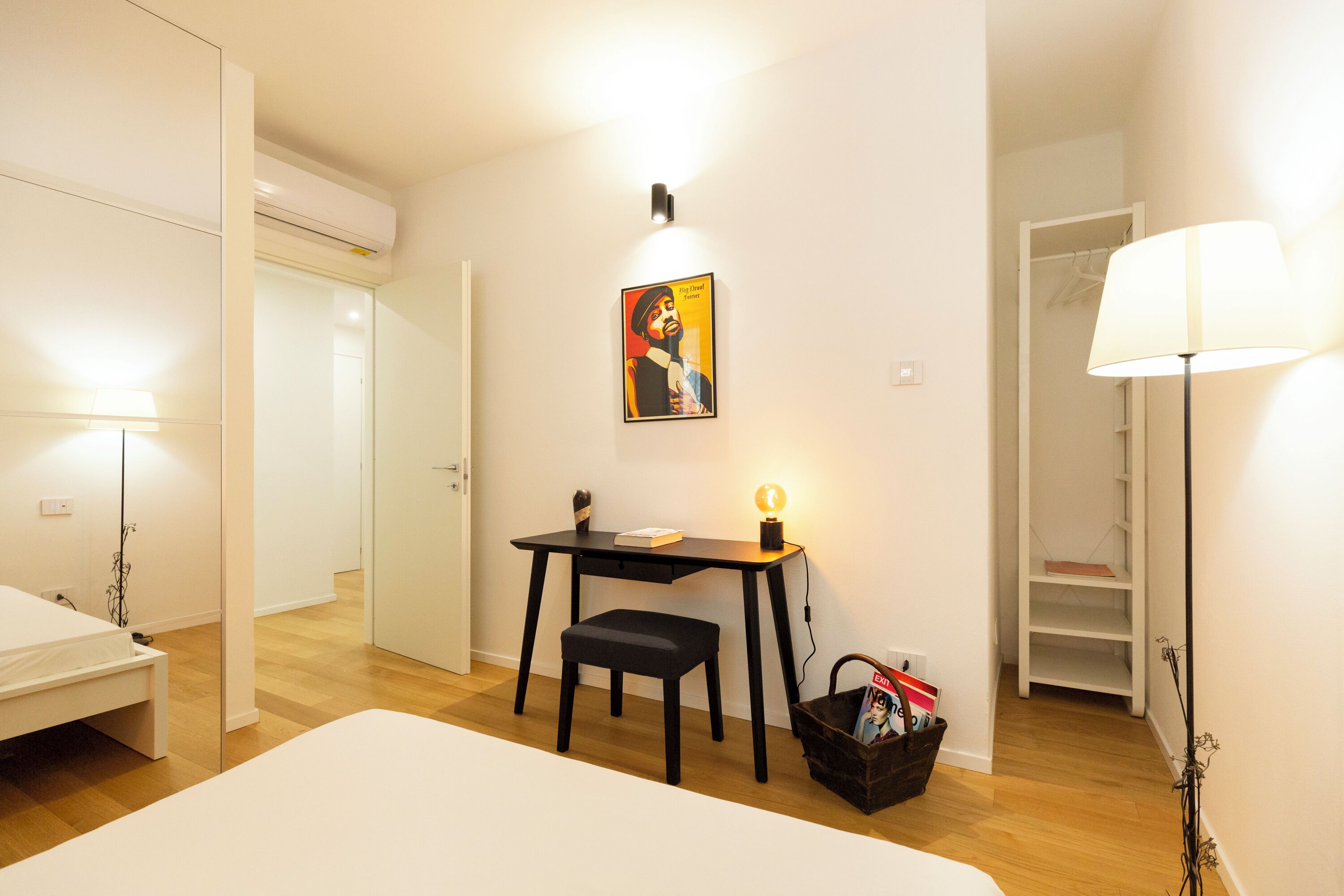 Ein Schlafzimmer mit einem Bett, einem Schreibtisch mit Stuhl, einer Lampe, einem Wandbild und einem Kleiderschrank.