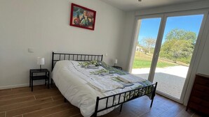 A bedroom with a bed, a nightstand, a painting, and a view through a sliding glass door.